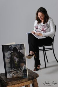 Arrière-plan : Nathalie Bagadey sur une chaise en train d'écrire. Premier plan : son livre Citara (tome 1) posé sur un tabouret.