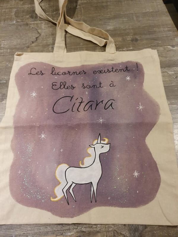 Tote bag représentant une licorne sur un fond mauve étoilé. Texte : "Les licornes existent ! Elles sont à Citara."