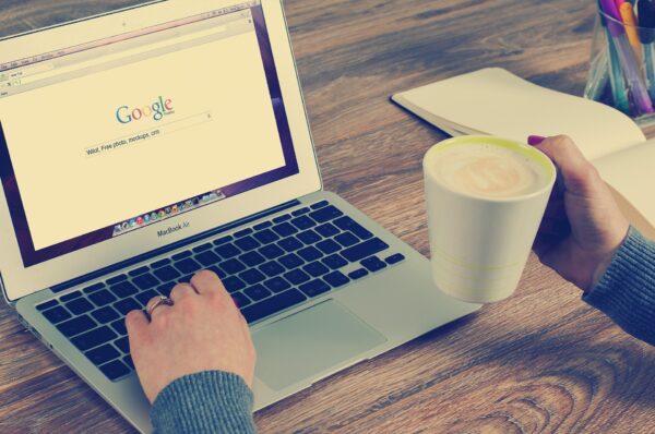 image représentant un ordinateur ouvert sur la page Google et une main tenant une tasse à café