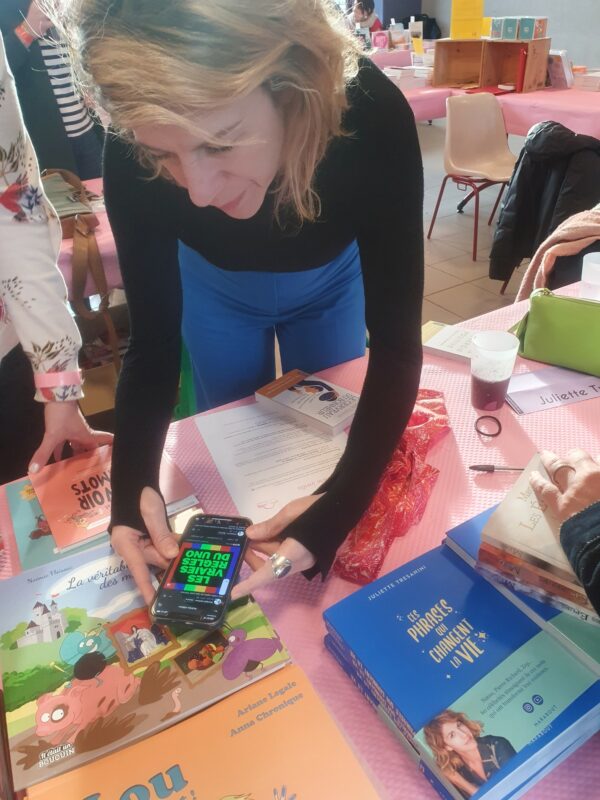 Photo de Juliette Tresanini en train de visionner une vidéo des règles du Uno (on lit le titre de la vidéo, "Les vraies règles du Uno" sur son téléphone).