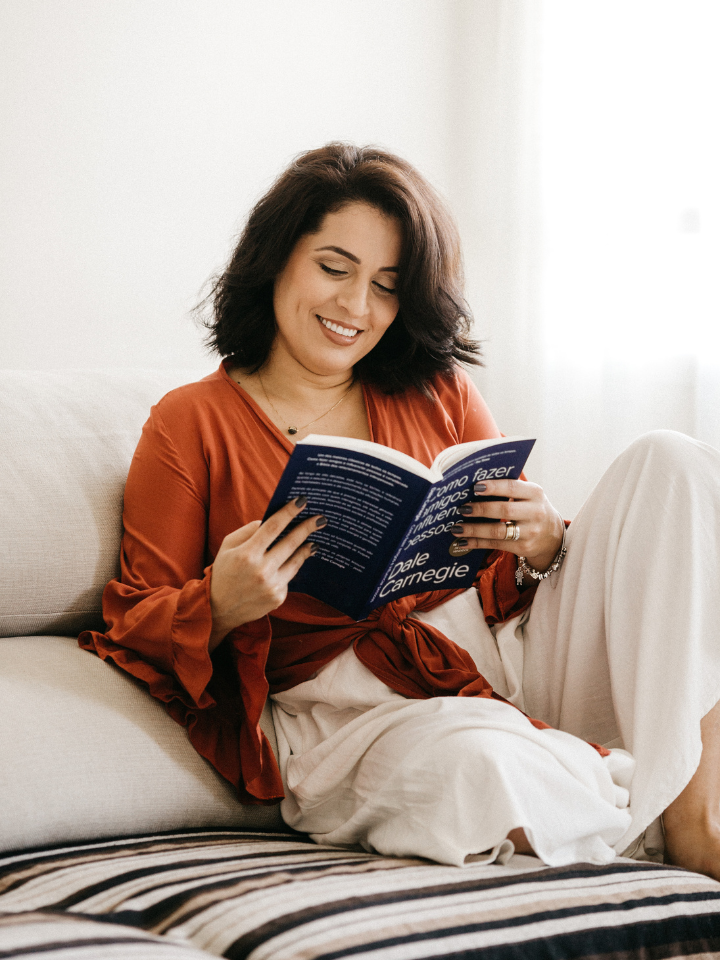 Femme assise sur un lit en train de lire le livre de Dale Carnegie.