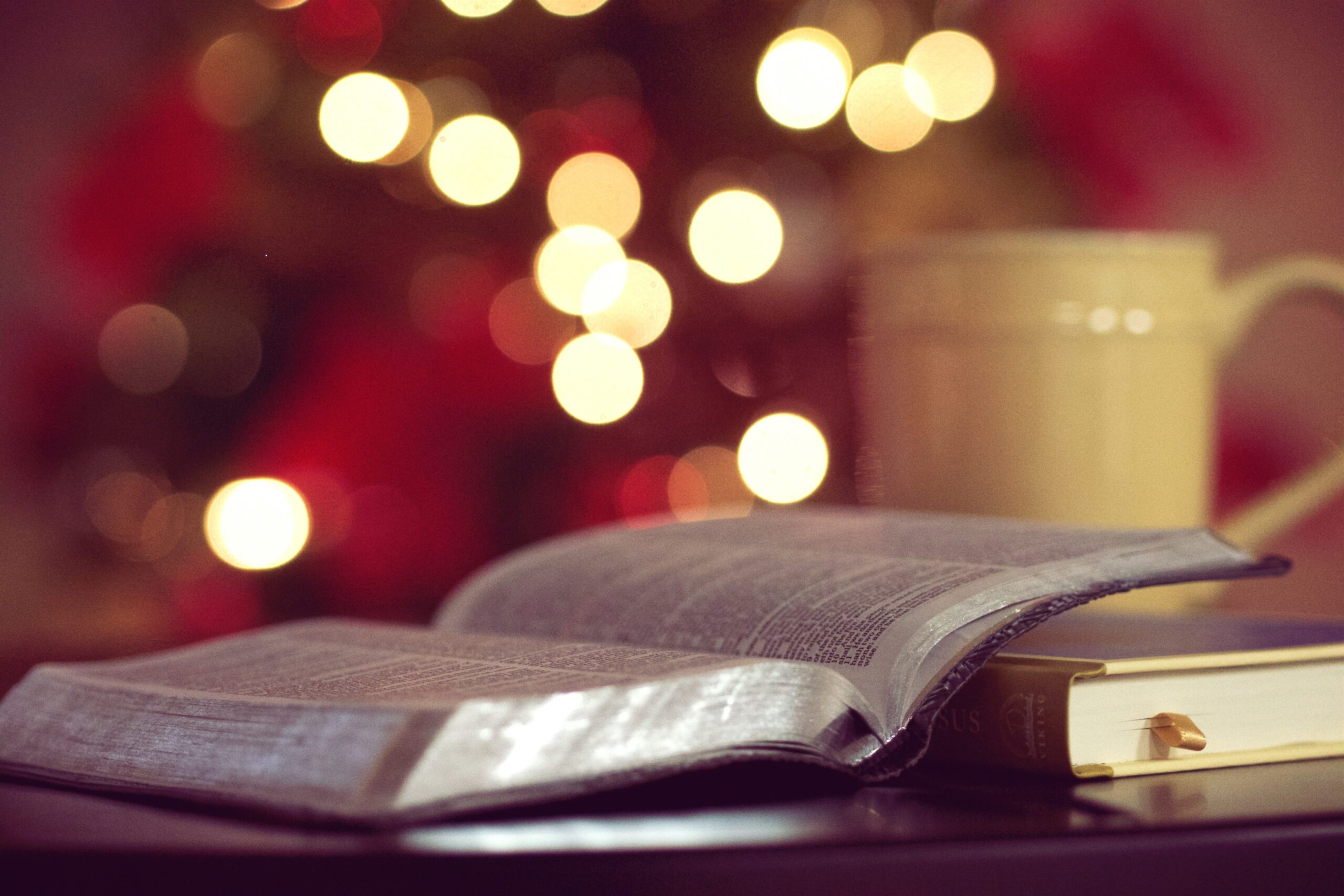 Photo de Aaron Burden sur Unsplash représentant un livre ouvert, une tasse de thé à côté, et de petites lumières en arrière plan