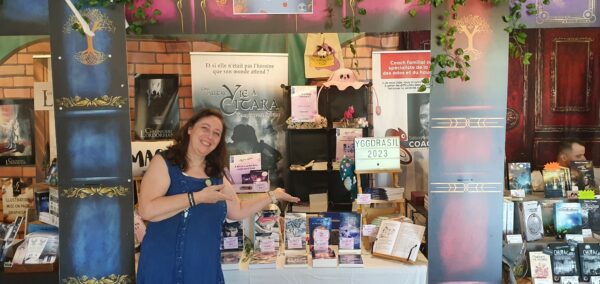 Fête du Chapelier - Nathalie Bagadey en tenue médiévale bleue montrant son stand.