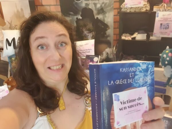 Fête du Chapelier - Nathalie Bagadey, en tenue grecque, l'air dépité, tenant son unique exemplaire de Kassandra et la Grèce des légendes en main