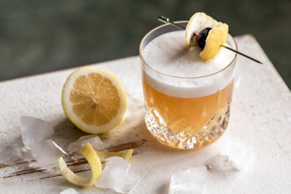 Un verre d'Amaretto Sour à côté d'1/2 citron et d'un zeste de citron.